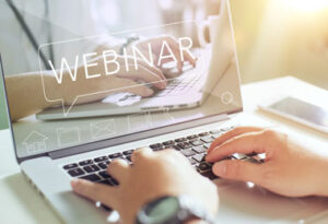 closeup of hands on a laptop keyboard with the word webinar on the screen